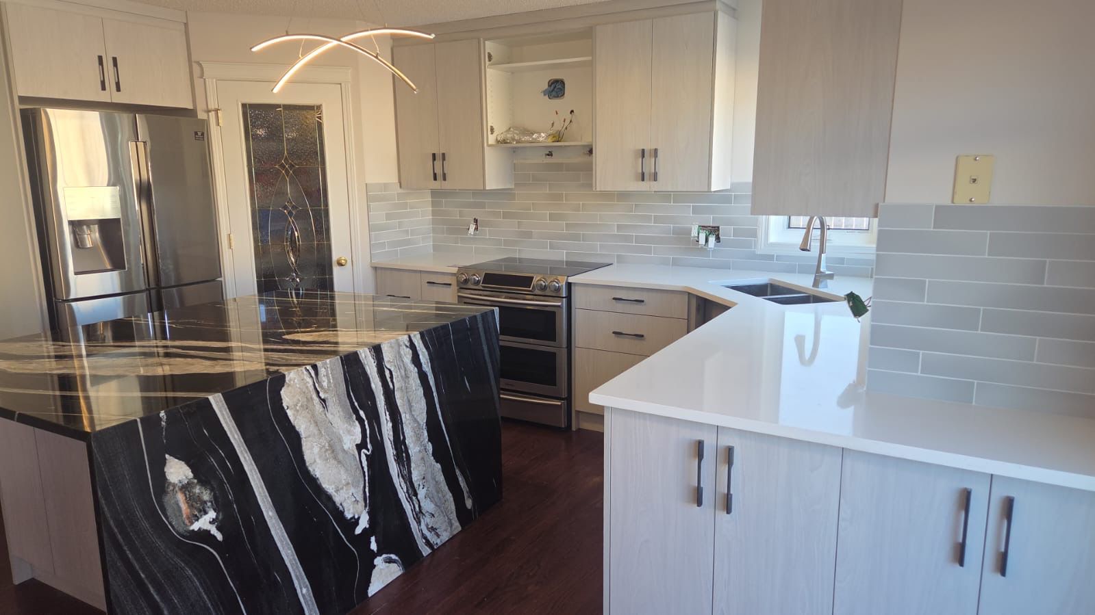 Renovated kitchen with a custom black granite waterfall-edge island and white cabinetry, fabricated by Diamond Granite & Quartz Corp